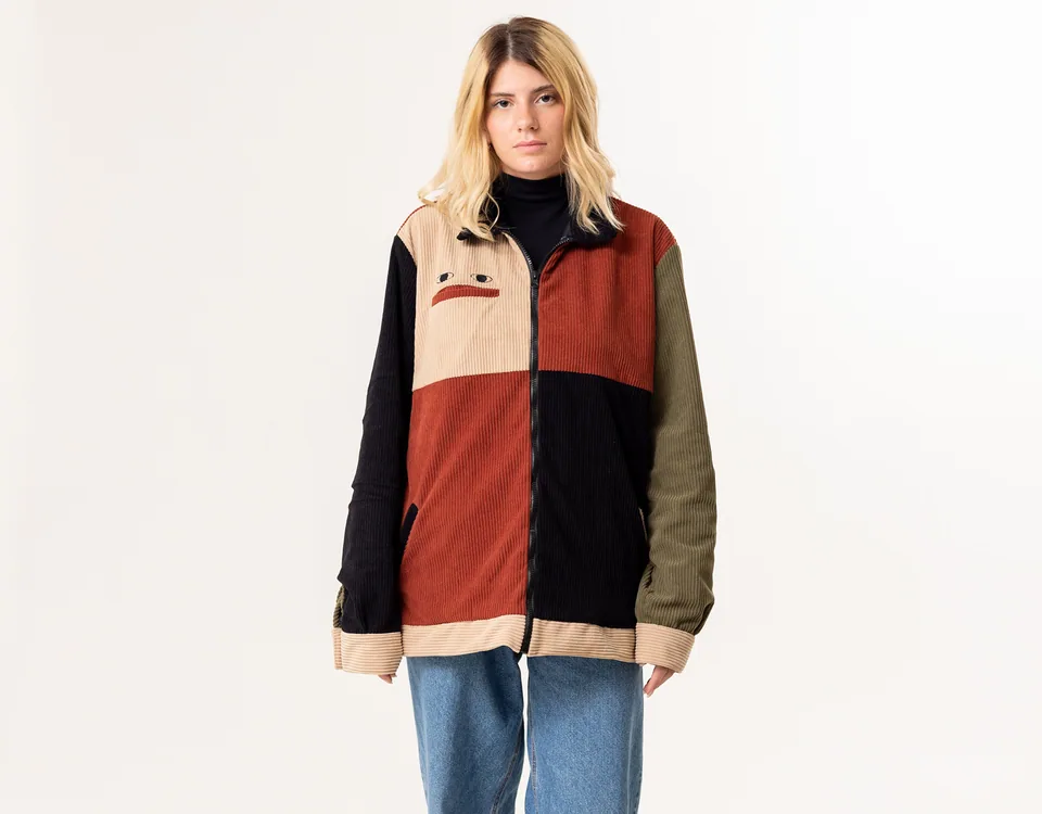 Model wearing a colour-block corduroy jacket with an embroidered face motif