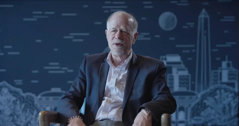 A guest interviewed at Monetarium 2 in front of the Washington skyline backdrop, a frame from the Highlights film